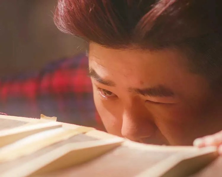 Luthier Isaac Jang inspects the details of an acoustic guitar back piece