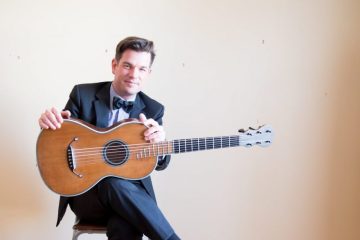 classical guitarist pascal valois sits in a chair with his guitar