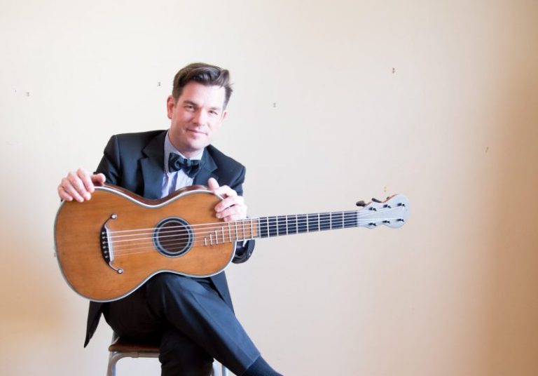 classical guitarist pascal valois sits in a chair with his guitar