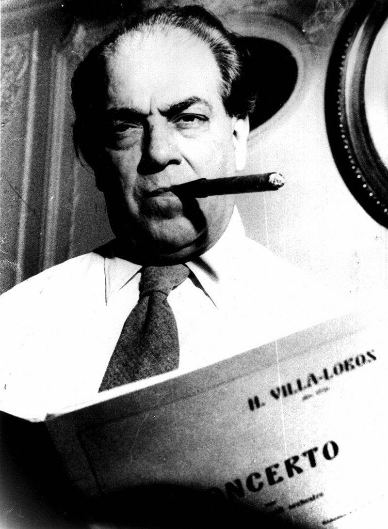 Composer and classical guitarist Heitor Villa-lobos smoking a cigar and holding a score of his concerto